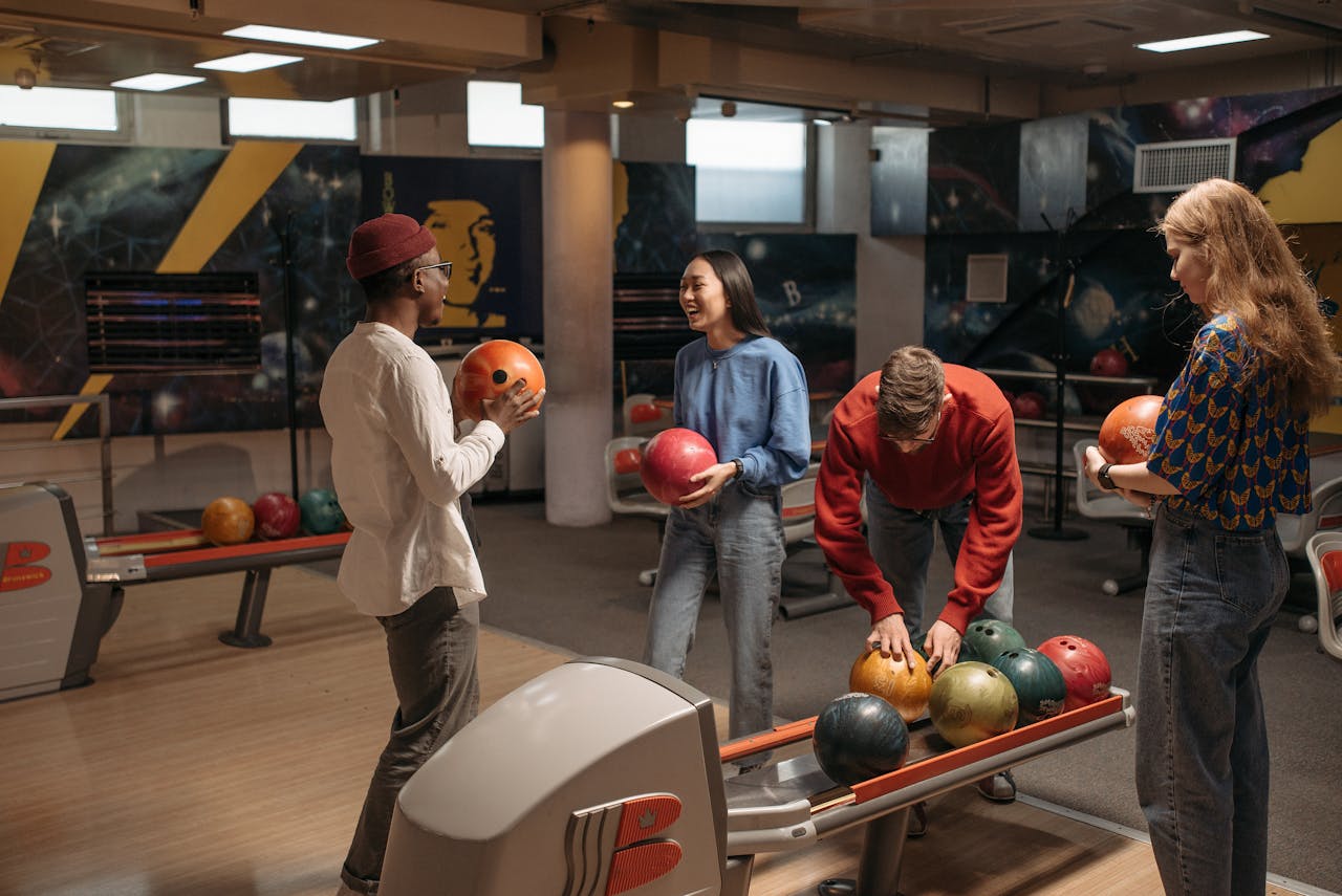 Four young people picking out types of bowling balls at an alley